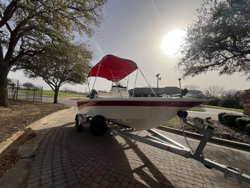 Slide: The Image of 2012 NauticStar 1810 boat with red canopy on trailer, parked under trees. - 34