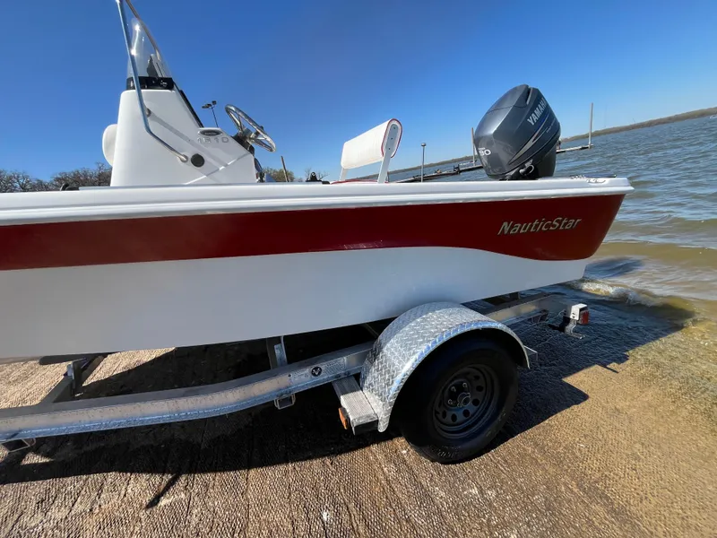 Slide: The Image of 2012 NauticStar 1810 boat on trailer by the water, featuring a red and white design. - 42