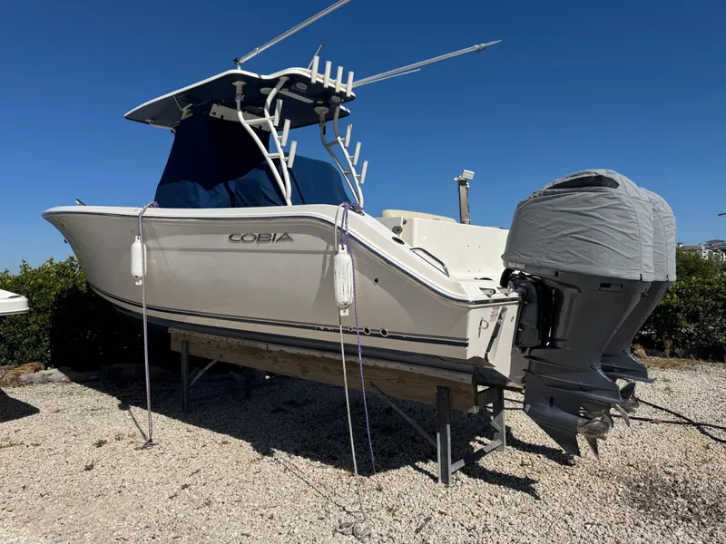 Slide: The Image of 2013 Cobia 296 Center Console boat on dry land, covered engine, clear blue sky. - 1