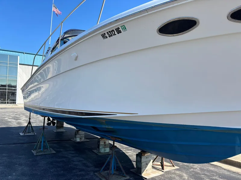 Slide: The Image of 1999 Sea Ray 370 Express Cruiser on stands, white hull with blue bottom, outdoors. - 2