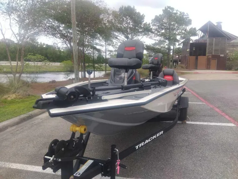 Slide: The Image of 2025 Tracker Pro Team 190 boat on trailer in parking lot, surrounded by trees. - 5