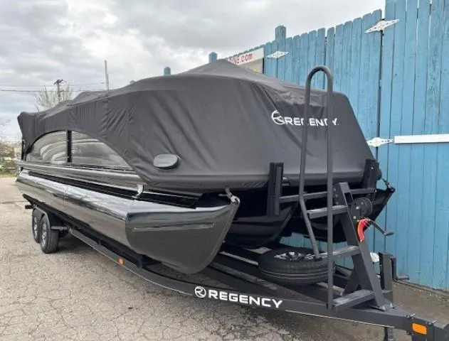 Slide: The Image of 2024 Regency 250 LE3 boat covered on trailer, parked near blue fence. - 48