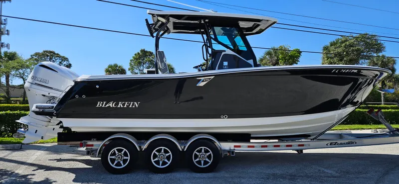 Slide: The Image of 2020 Blackfin 272 CC boat on a trailer, side view, black hull, triple-axle trailer. - 0