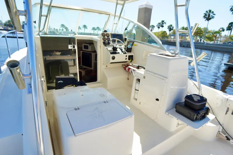 Slide: The Image of 2003 Pursuit 3070 Express boat interior with helm, seating, and storage, docked by palm trees. - 34