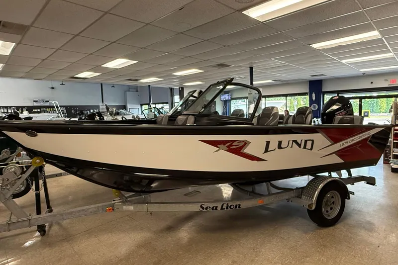 The Image of 2025 Lund 1875 Crossover XS boat displayed indoors on a trailer. - 0