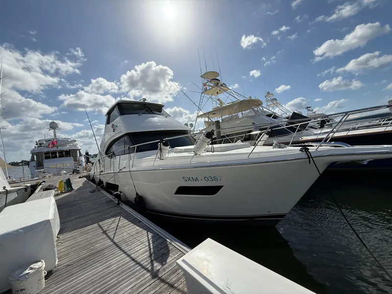 Slide: The Image of 2022 Riviera 54 Enclosed Flybridge yacht docked under a sunny sky. - 0