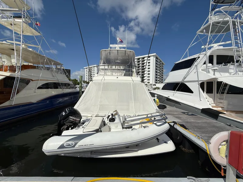 Slide: The Image of 2022 Riviera 54 Enclosed Flybridge yacht docked with inflatable boat, surrounded by other yachts. - 1