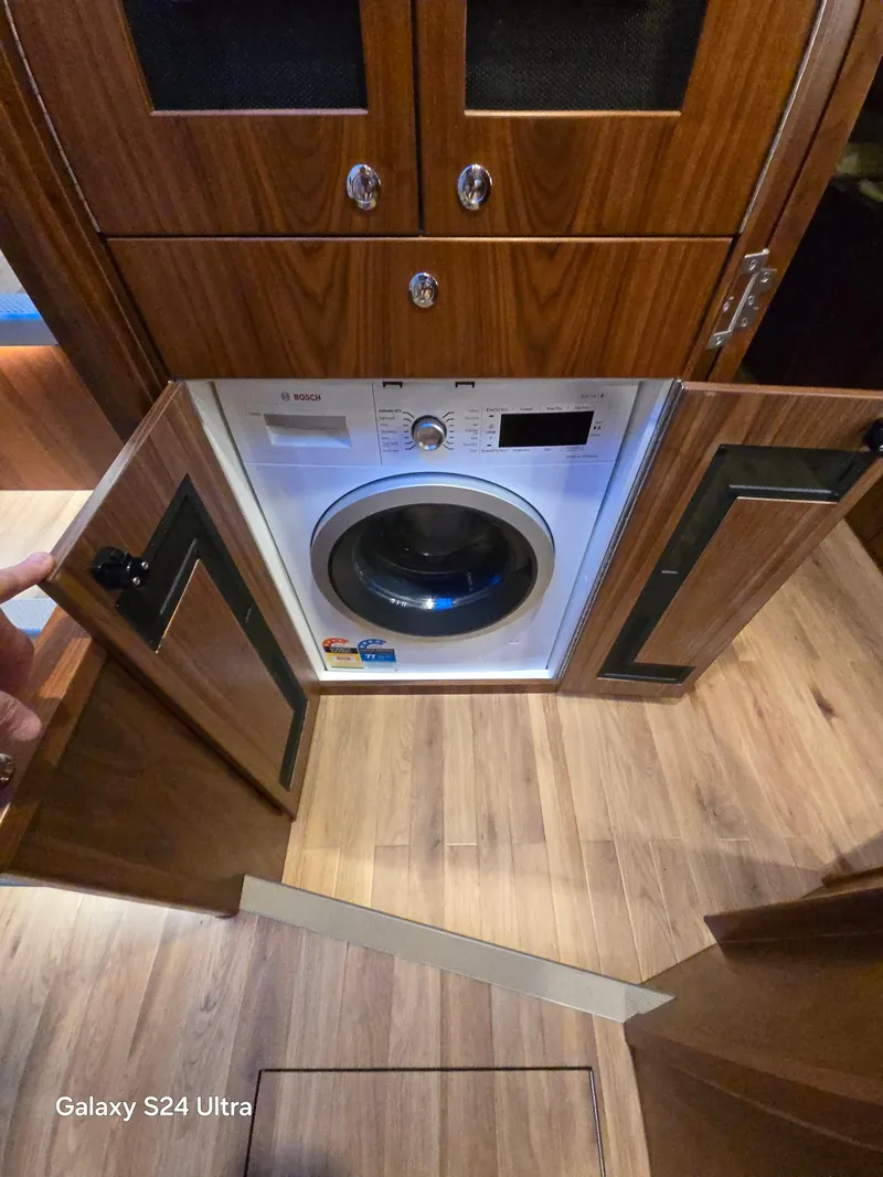 Slide: The Image of 2022 Riviera 54 Enclosed Flybridge interior with built-in washing machine and wooden cabinetry. - 12