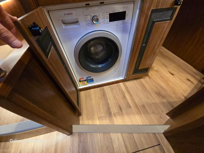 Slide: The Image of Washing machine inside 2022 Riviera 54 Enclosed Flybridge, wooden cabinetry, and flooring. - 13