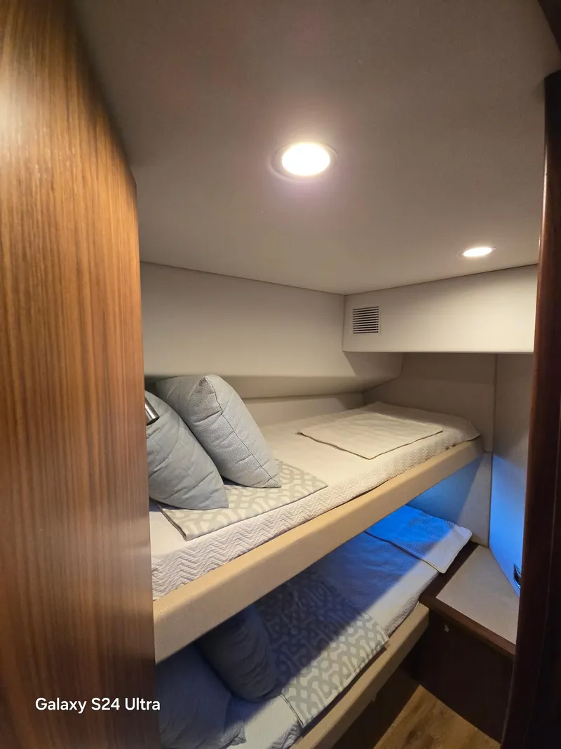 Slide: The Image of Interior of 2022 Riviera 54 Enclosed Flybridge with cozy bunk beds and soft lighting. - 16