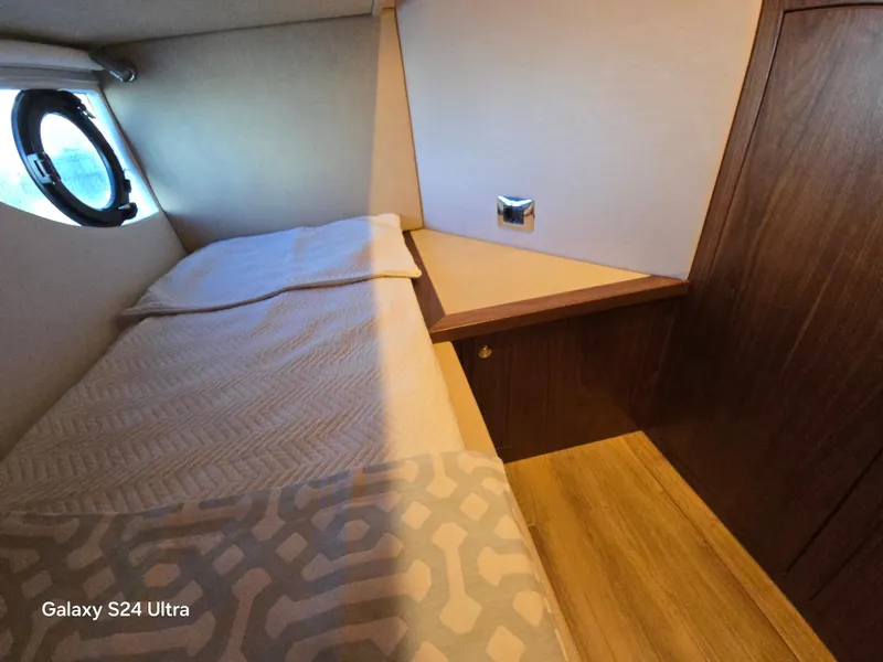 Slide: The Image of 2022 Riviera 54 Enclosed Flybridge cabin interior with bed and porthole window. - 21