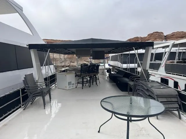 Slide: The Image of 2007 Lakeview houseboat deck with canopy, chairs, and table, docked near rocky landscape. - 15