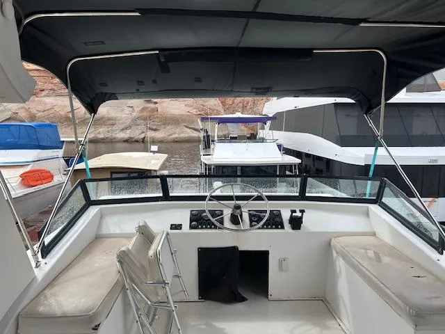 Slide: The Image of 2007 Lakeview Houseboat interior with steering wheel, seating, and canopy, docked near rocky shoreline. - 16