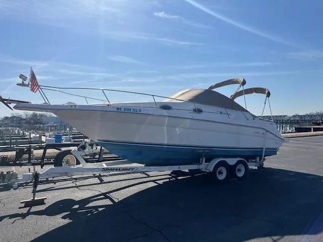 The Image of 1996 Sea Ray 270 Sundancer boat on trailer, parked at marina under clear blue sky. - 1