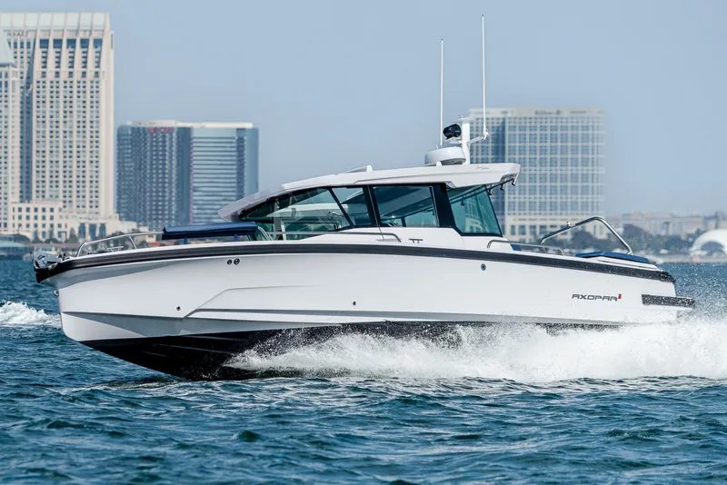 Slide: The Image of 2025 Axopar 29XC Cross Cabin Aft Cabin cruising in sunny waters near a marina. - 2