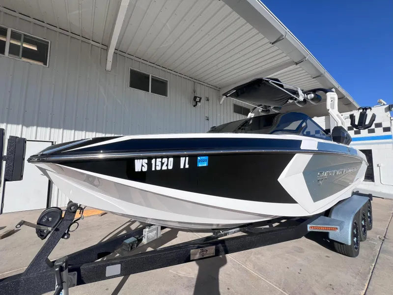 Slide: The Image of 2019 Nautique Super Air Nautique G25 boat on trailer, parked outside a building. - 2