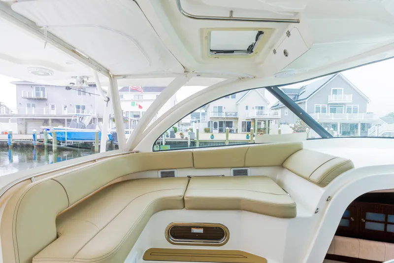 Slide: The Image of 2018 Pursuit OS 385 Offshore boat interior with beige seating, docked near waterfront homes. - 10