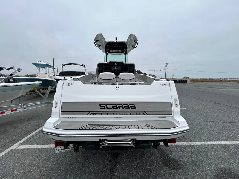 Slide: The Image of 2020 Scarab 255 Open ID boat, rear view, parked on asphalt, overcast sky. - 13