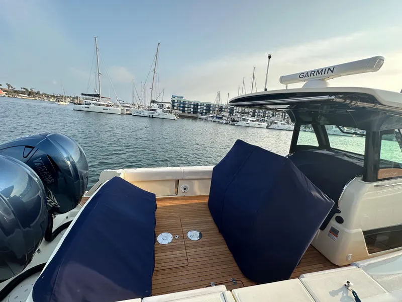 Slide: The Image of The image shows the stern of a 2021 Chris-Craft Catalina 34. It features two large outboard engines and a spacious seating area with blue covers. Yachts are visible in the harbor background. - 35