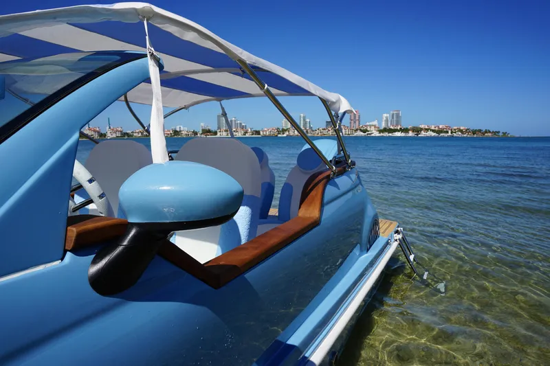 Slide: The Image of 2025 Car Off-shore Fiat 500 Classic on water, blue sky, city skyline in background. - 13
