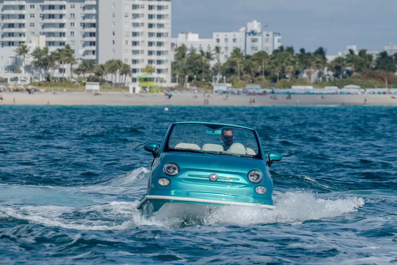 Slide: The Image of 2025 Car Off-shore Fiat 500 Classic driving on water near a coastal city. - 5