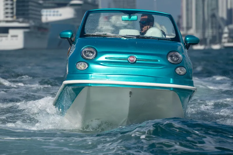 Slide: The Image of Amphibious 2025 Fiat 500 Classic navigating water, cityscape in background. - 3