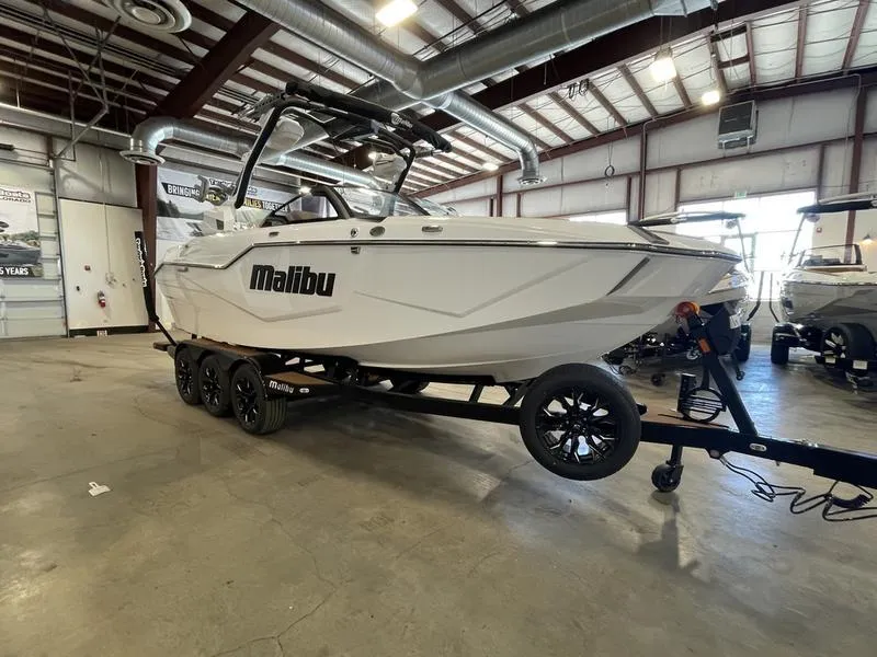 Slide: The Image of 2025 Malibu M230 boat in showroom, white exterior, on trailer, industrial setting. - 5