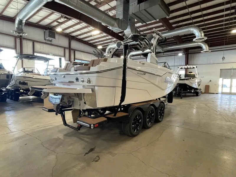 Slide: The Image of 2025 Malibu M230 boat in showroom, triple-axle trailer, industrial setting. - 6