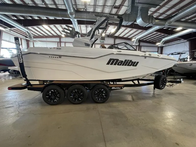 Slide: The Image of 2025 Malibu M230 boat in showroom, white exterior, on a trailer with black wheels. - 7