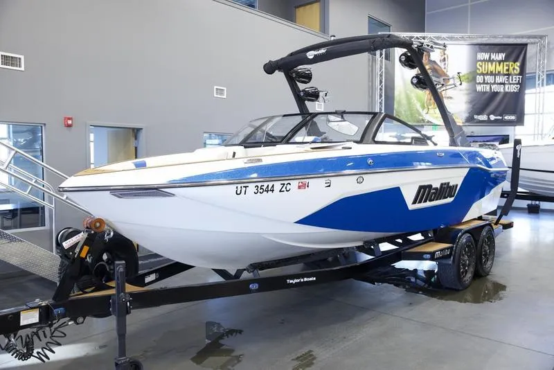 Slide: The Image of 2024 Malibu 23 LSV boat on trailer in showroom, blue and white design. - 5