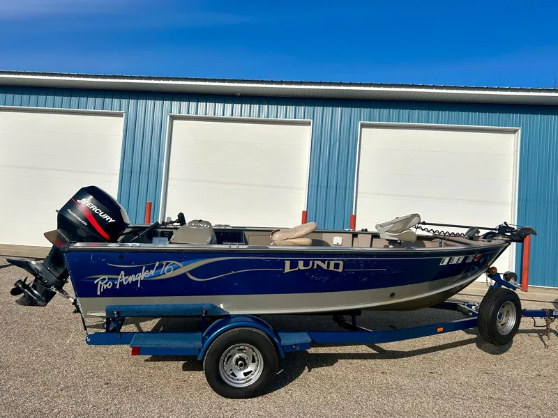 Slide: The Image of 2002 Lund Pro Angler 16 boat on trailer, blue exterior, parked near blue garage doors. - 0