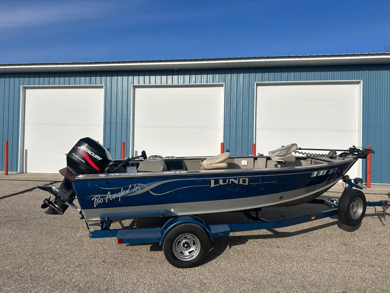Slide: The Image of 2002 Lund Pro Angler 16 boat on trailer, parked in front of blue storage units. - 2