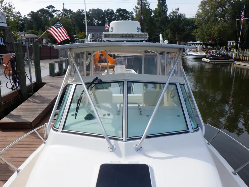 Slide: The Image of 1999 Pursuit 2870 Walkaround boat docked, featuring American flag and clear windshield. - 14