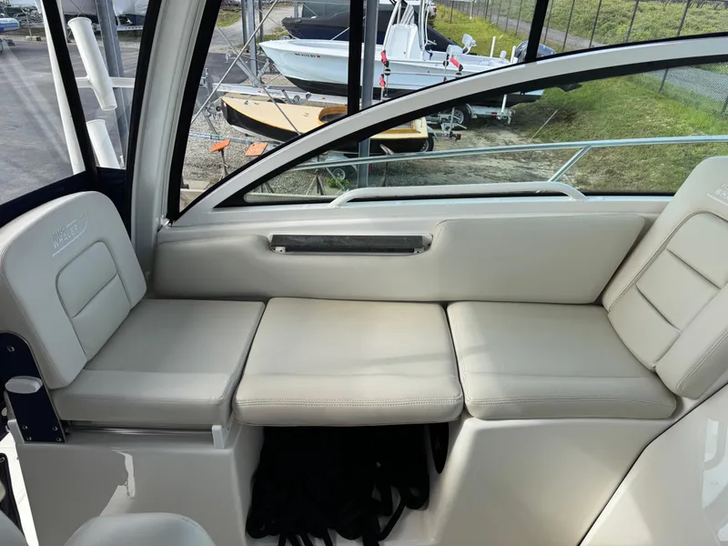Slide: The Image of 2022 Boston Whaler 285 Conquest interior seating with beige cushions and window view. - 17