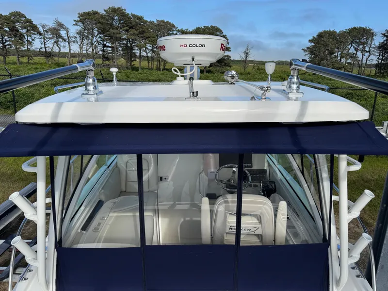 Slide: The Image of 2022 Boston Whaler 285 Conquest boat with radar, blue canopy, and lush background. - 8