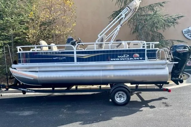 Slide: The Image of 2025 Sun Tracker Bass Buggy 18 DLX pontoon boat on trailer, parked outdoors. - 0