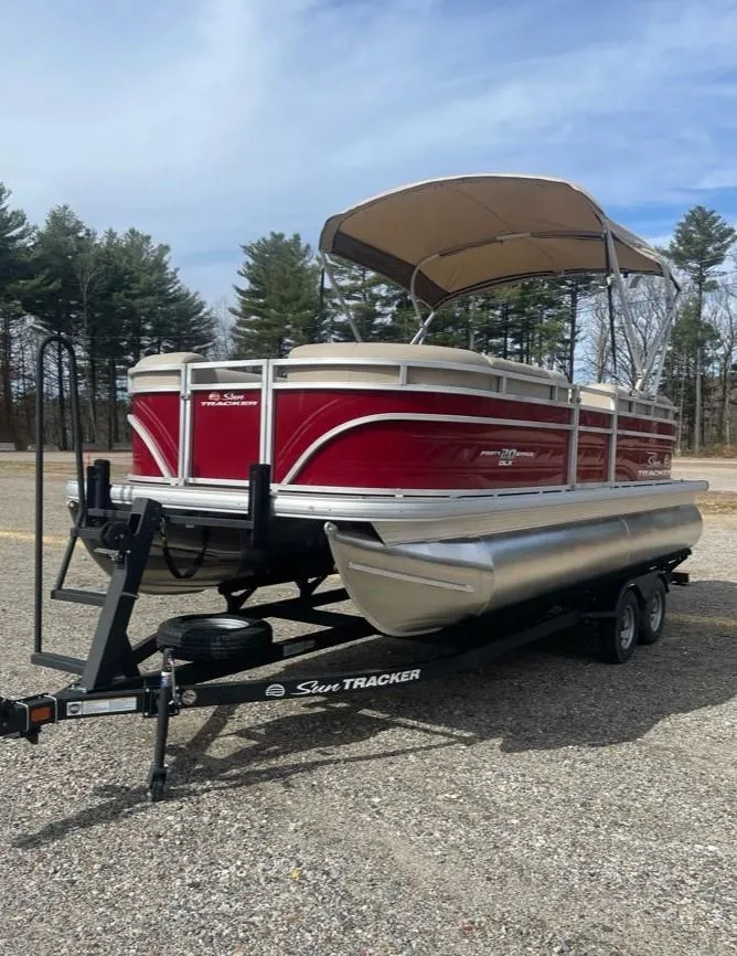 Slide: The Image of 2025 Sun Tracker Party Barge 20 DLX pontoon boat on trailer, parked outdoors. - 2
