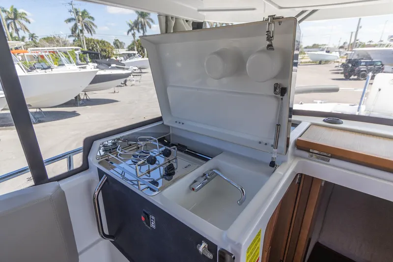 Slide: The Image of 2022 Jeanneau NC Sport 895 boat kitchen with stove and sink, docked outdoors. - 25