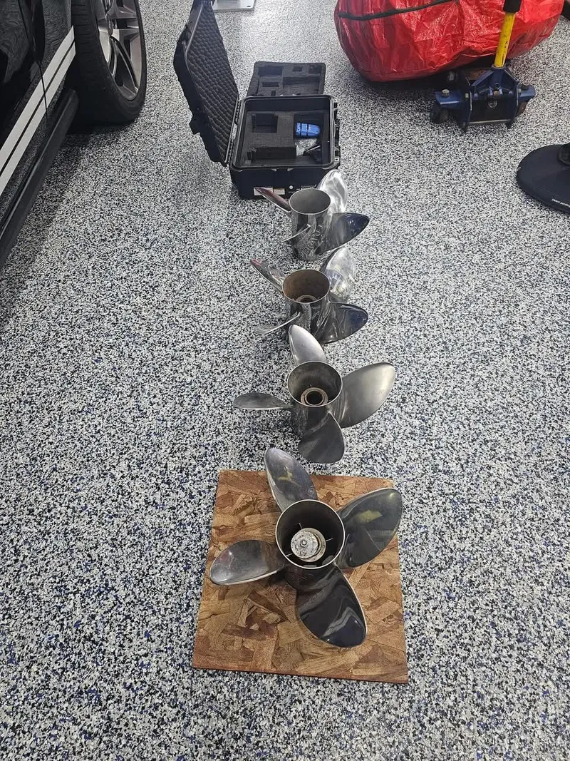 Slide: The Image of Four stainless steel boat propellers on a speckled garage floor, near a 2003 Ultimate Warlock 29 World Class Offshore Race. - 44