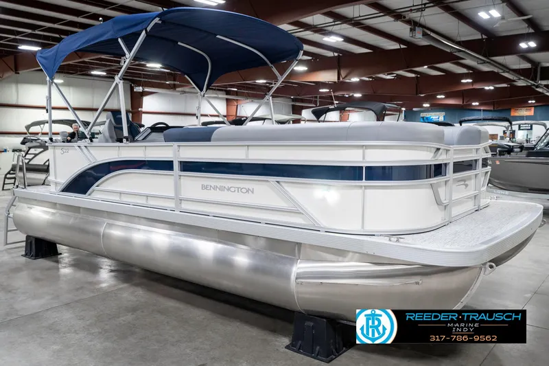 Slide: The Image of 2025 Bennington 22 SLS pontoon boat with blue canopy in indoor showroom. - 5