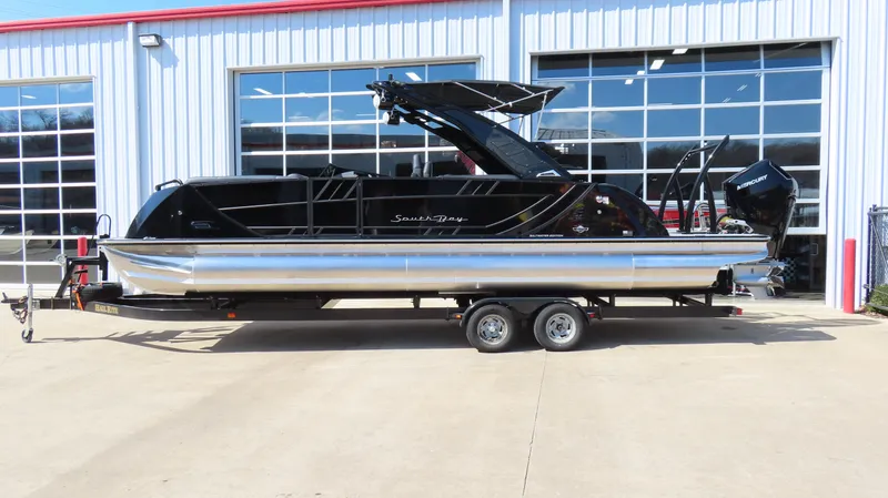 The Image of 2025 South Bay 25 Sport CR9 3 pontoon boat on trailer, parked outside a garage. - 0
