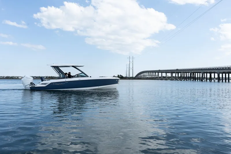 Slide: The Image of 2025 Monterey Elite 27 OB boat cruising on a calm lake near a bridge under a blue sky. - 39