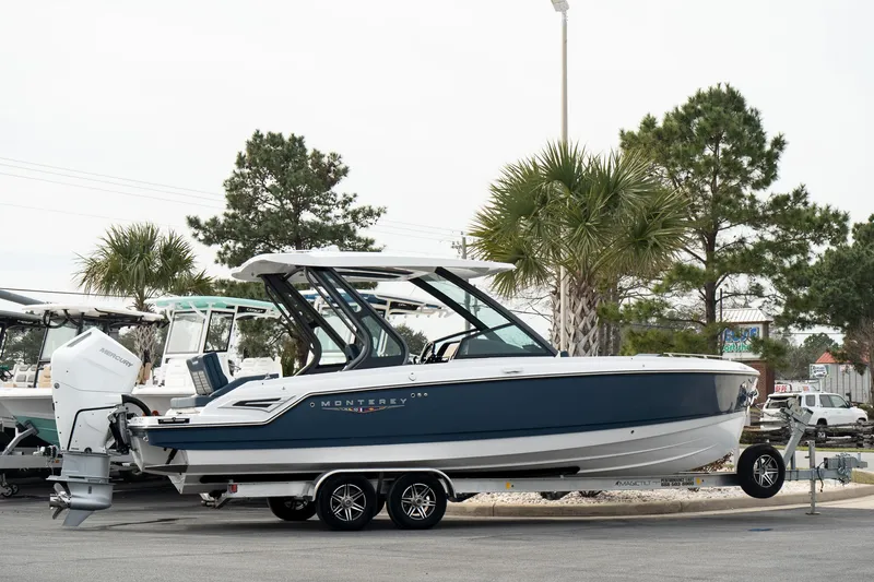 Slide: The Image of 2025 Monterey Elite 27 OB boat on trailer, parked outdoors with trees in background. - 7