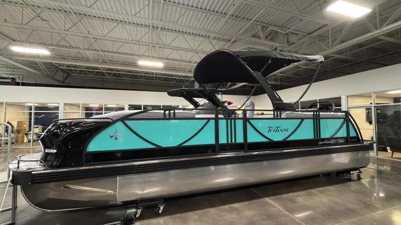 Slide: The Image of 2025 JC Sporttoon 26TT pontoon boat with teal accents in a showroom. - 1