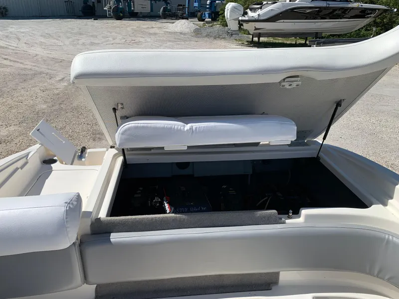 Slide: The Image of 2009 Bayliner 205 boat with open storage compartment, white seating, and visible engine area. - 10