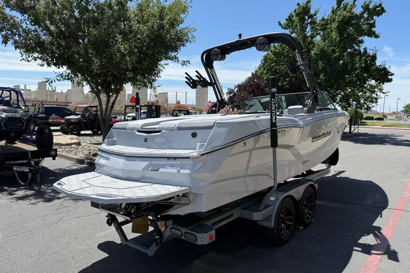 Slide: The Image of 2025 MasterCraft NXT24 boat on trailer, parked outdoors under trees. - 15