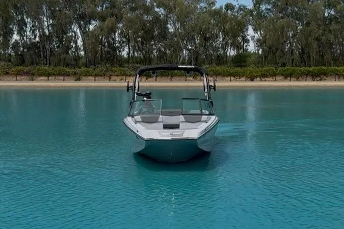 Slide: The Image of 2025 MasterCraft NXT24 boat on serene blue water with tree-lined shore. - 4