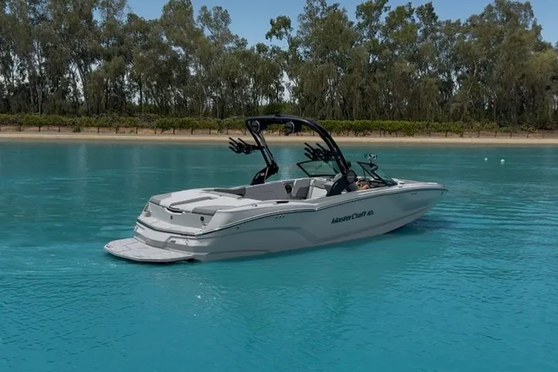 Slide: The Image of 2025 MasterCraft NXT24 boat on serene blue water, surrounded by lush trees. - 7