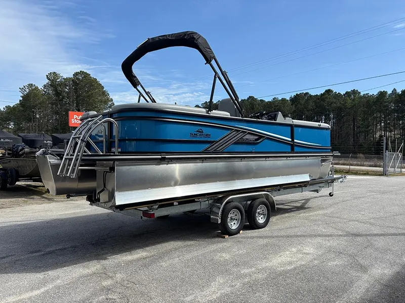 Slide: The Image of 2025 SunCatcher Fusion 324RC pontoon boat on trailer, blue and silver design, parked outdoors. - 7