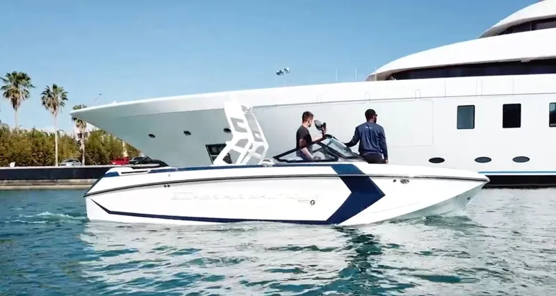 Slide: The Image of 2020 Nautique Super Air G23 boat on water, with two people onboard, near a large yacht. - 2